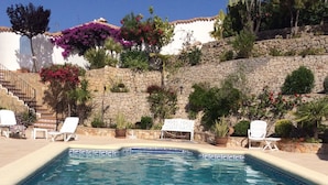A rectangular pool with clear blue water, surrounded by white lounge chairs and a stone wall with plants. - Secluded, Spacious, Luxury Villa & Swimming Pool in Beautiful Rustic Location  (Benidoleig)