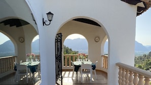 A covered terrace with a table set for dining, a view of mountains, and a white wall with a decorative archway. - Secluded, Spacious, Luxury Villa & Swimming Pool in Beautiful Rustic Location  (Benidoleig)