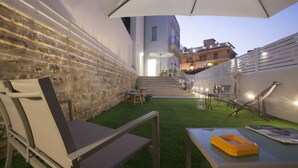 A patio with a stone wall, a grassy area, a table with a yellow tray, and a chair. - Funduq iblea hospitality - ground floor apartment (Pozzallo)