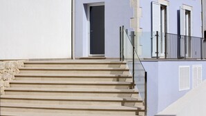 A building with a set of beige stone steps leading to a door, a balcony with a glass railing, and a light blue facade. - Funduq iblea hospitality - ground floor apartment (Pozzallo)
