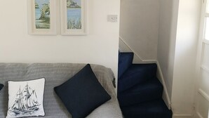 A room with a sofa, two framed pictures, a staircase, and a door. - Cosy & Comfortable Entire Holiday Home, Llanelli. Fully equipped. Dog friendly (Llanelli)