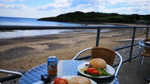 A table with a drink, burger, and salad, overlooking a beach with a distant view of a hill. - Cosy & Comfortable Entire Holiday Home, Llanelli. Fully equipped. Dog friendly (Llanelli)