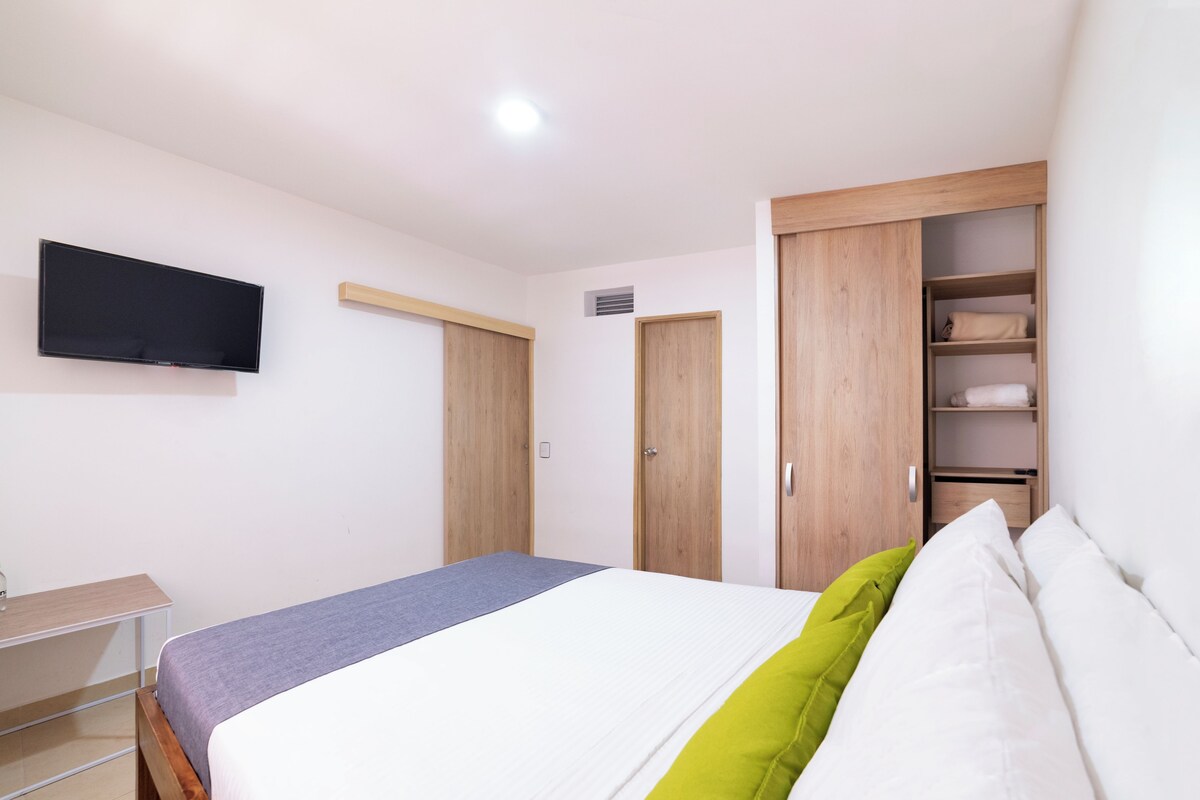 A bedroom with a bed, a TV mounted on the wall, and wooden wardrobes.