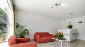 Un salon moderne avec un canapé rouge, une table basse blanche et un comptoir d’accueil agrémenté d’une plante en pot.
