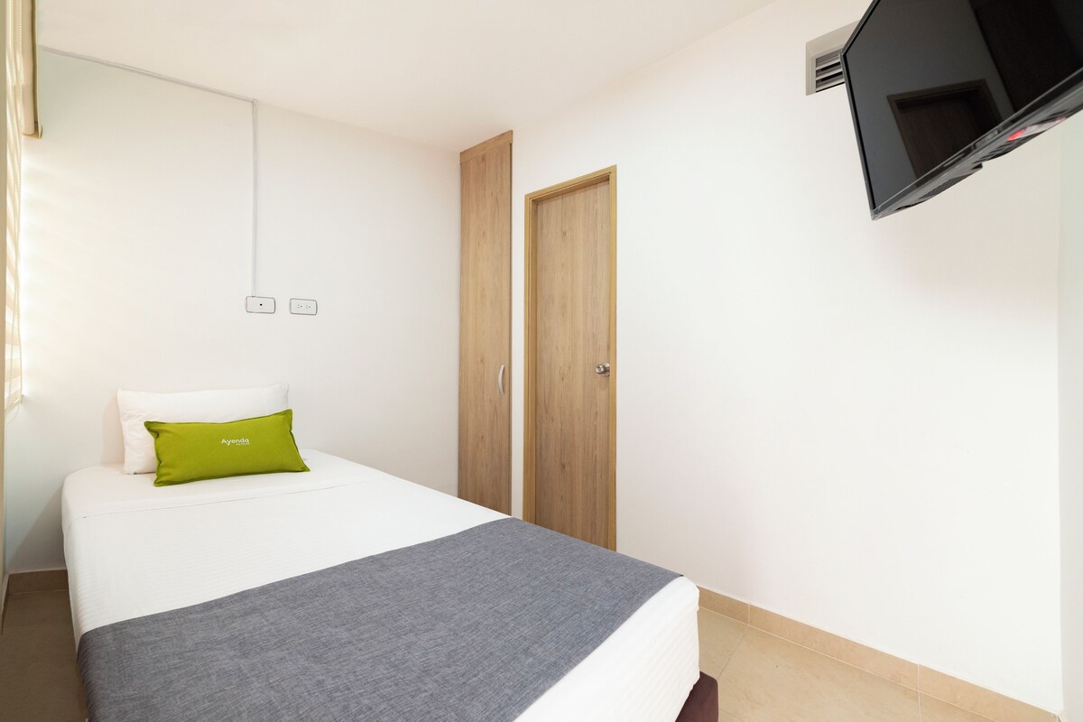 A bedroom with a bed, a TV mounted on the wall, and a wooden wardrobe.
