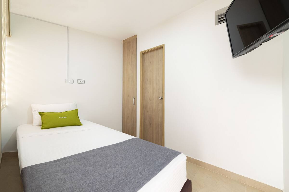 A hotel room with a bed, a TV mounted on the wall, and a wooden wardrobe.