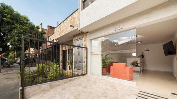 Un bâtiment moderne avec une façade en pierre, une entrée en verre et un petit espace extérieur aménagé avec des chaises orange.
