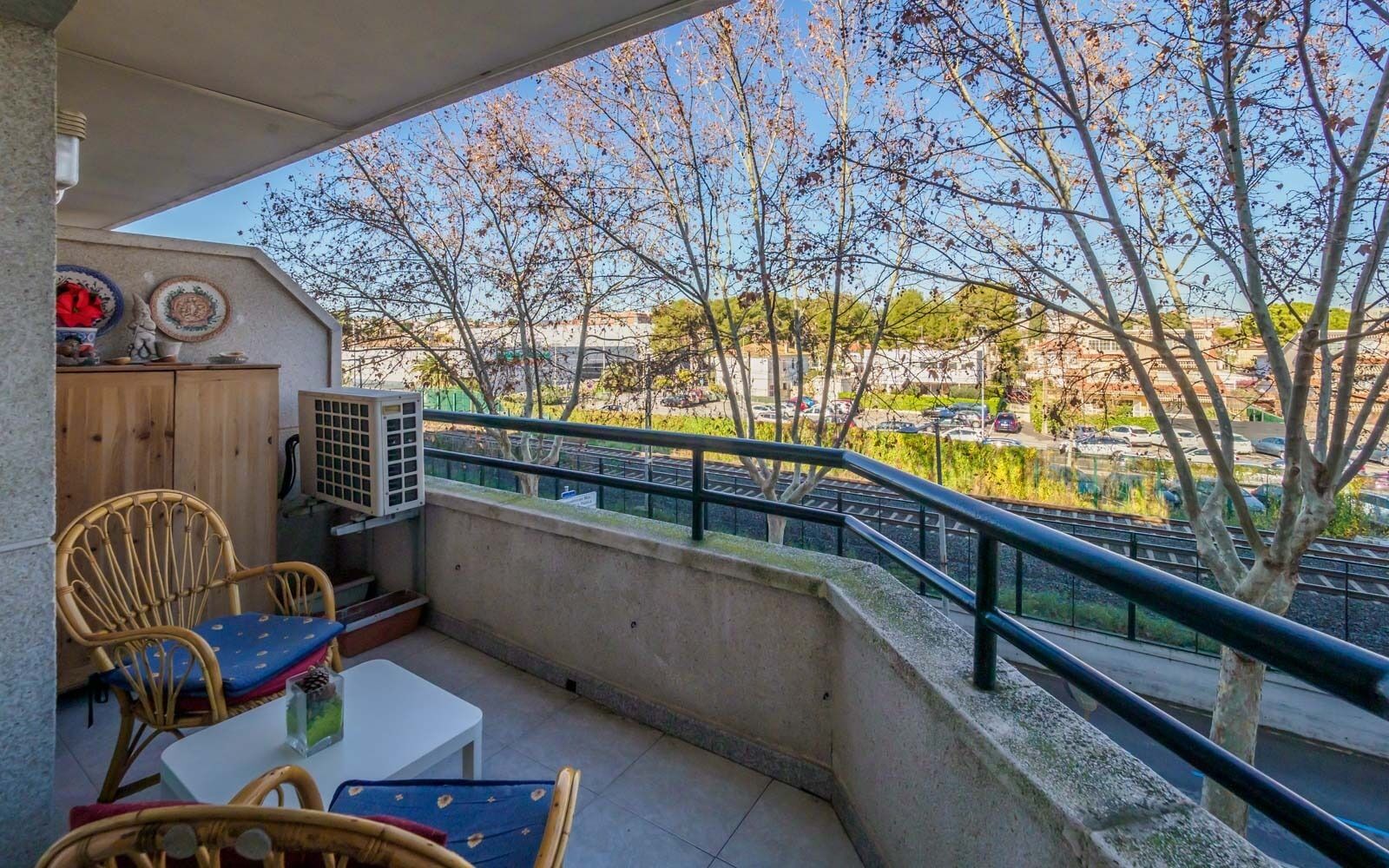 A balcony with a table and chairs, a wooden cabinet, and an air conditioning unit.