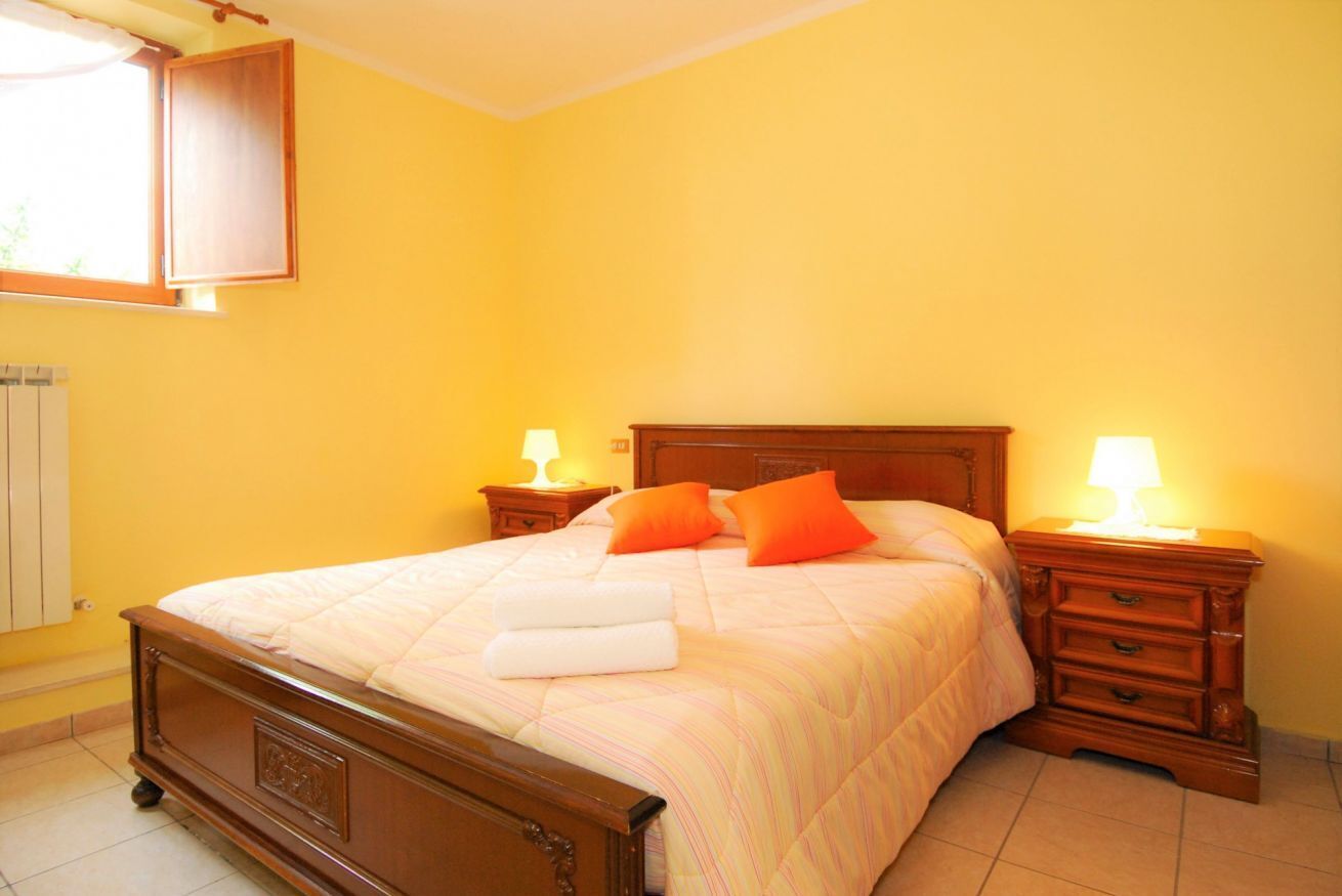 A bedroom with a wooden bed, two bedside tables with lamps, and a window with a curtain.