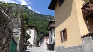 A narrow street with buildings on either side, a stone wall on the left, and a mountain in the background. - Mount N Lake Apartment -Ledro Garda (Ledro)