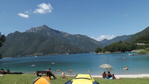 A lakeside campsite with tents, people swimming and relaxing, and mountains in the background. - Mount N Lake Apartment -Ledro Garda (Ledro)