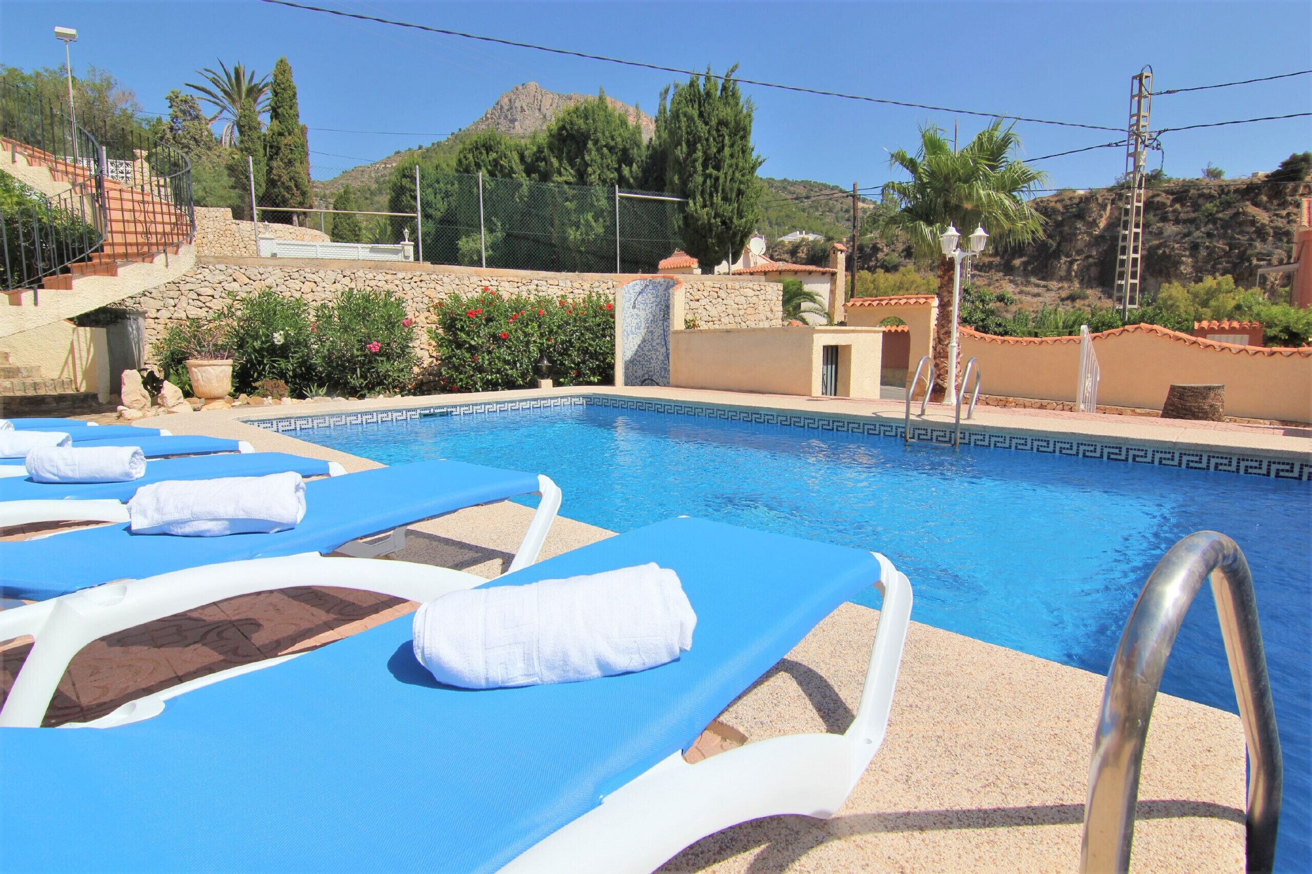 A pool area with blue lounge chairs and white towels, surrounded by a stone wall and greenery.