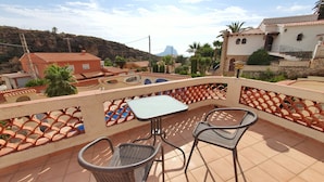 A terrace with a table and two chairs, overlooking a residential area with houses and a mountain in the background.