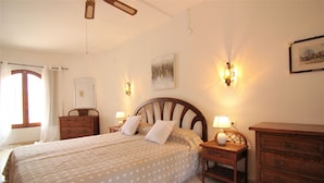 A bedroom with a bed, bedside tables, a dresser, a ceiling fan, and wall sconces.