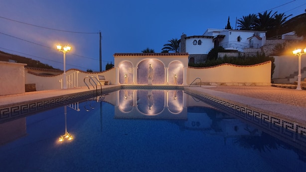 A swimming pool with a reflection of a building facade, surrounded by walls and two street lamps.