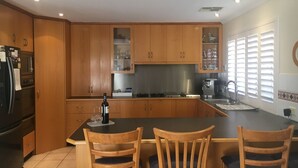 Ett kök med träskåp, ett svart kylskåp, en kaffebryggare och en matplats med två trästolar.