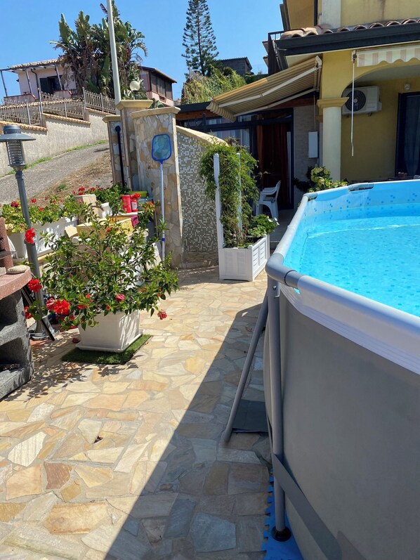 A swimming pool with a stone patio, potted plants, and a view of a hillside.