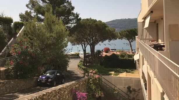 Una calle costera con un coche estacionado, árboles y un edificio con balcón con vistas al mar.