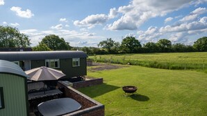 A green mobile home with a patio area, including a table and chairs, and a fire pit in a grassy yard.
