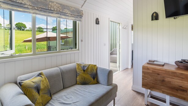 A room with a grey sofa, a wooden side table, and a TV mounted on the wall.