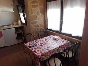 Ein Essbereich mit einem Tisch, der mit einer floralen Tischdecke bedeckt ist, vier Stühlen, einem kleinen Kühlschrank und einer Steinwand.