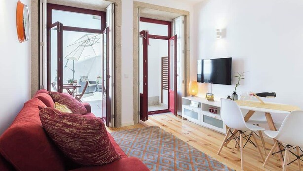 A modern living room with a red sofa, a wooden dining table with chairs, a TV, and a large window with a view of a crane.