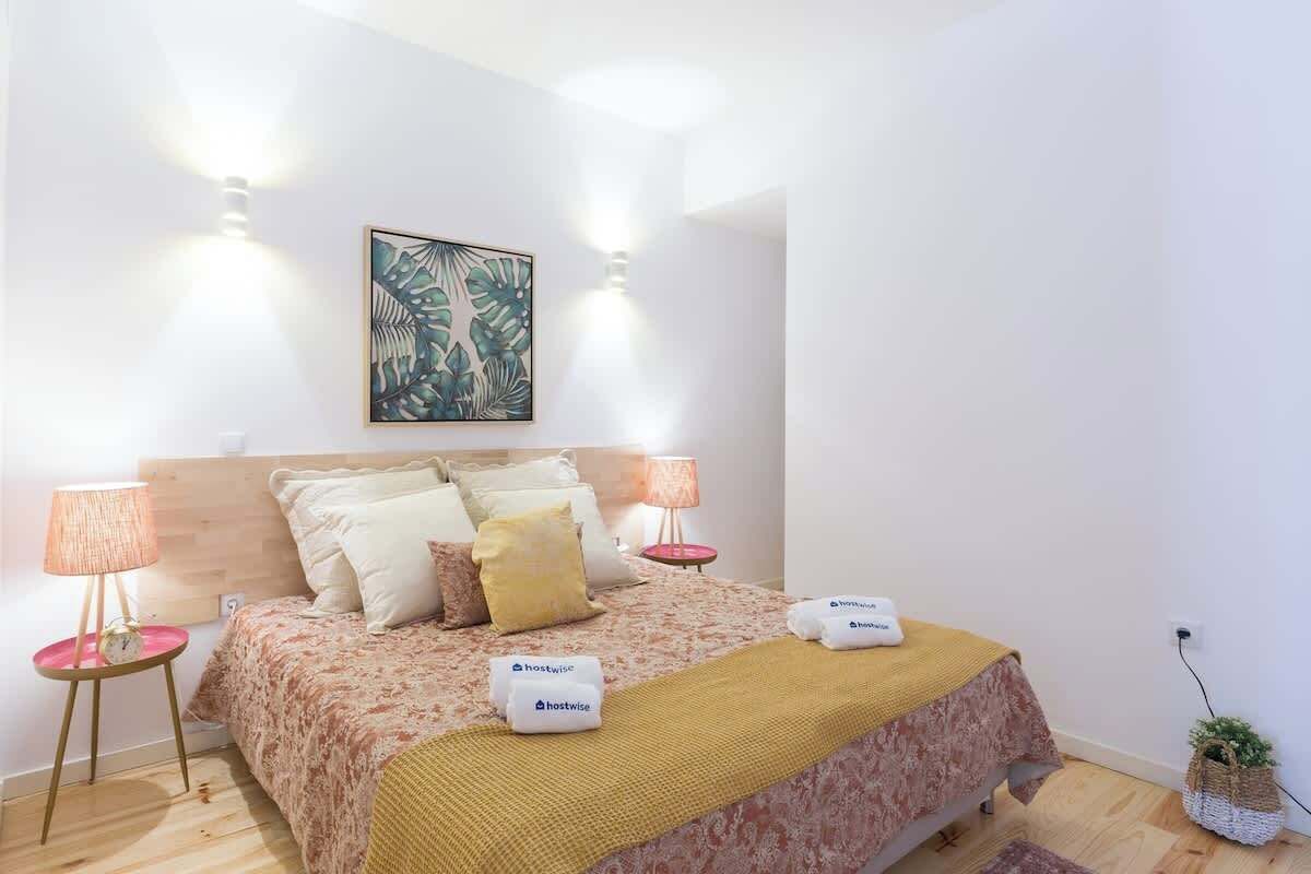 A neatly arranged bedroom with a bed, two bedside tables, a wall-mounted lamp, and a framed artwork above the bed.