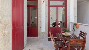 A wooden table with chairs, a red door, and a potted plant.