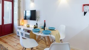 A dining area with a table set for four, a television mounted on the wall, and a red door.