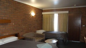 Quarto de hotel com parede de tijolos, uma cama grande, duas camas menores, uma mesa redonda e uma porta.
