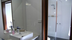 Casa de banho com lavatório branco, espelho e área de duche.