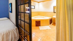 Habitación de hotel con cama, un ventanal con persianas, bañera y zona de ducha.