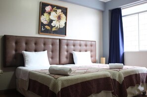 A double bed with a brown headboard, a floral painting above it, and a window with blue curtains. - Gran Hotel Villa del Sur (San Vicente de Cañete)