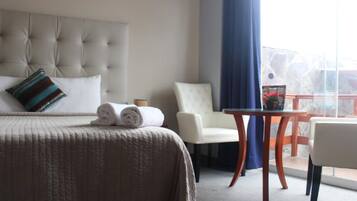 Habitación de hotel con una cama grande, una silla, una mesita y un balcón con vistas.