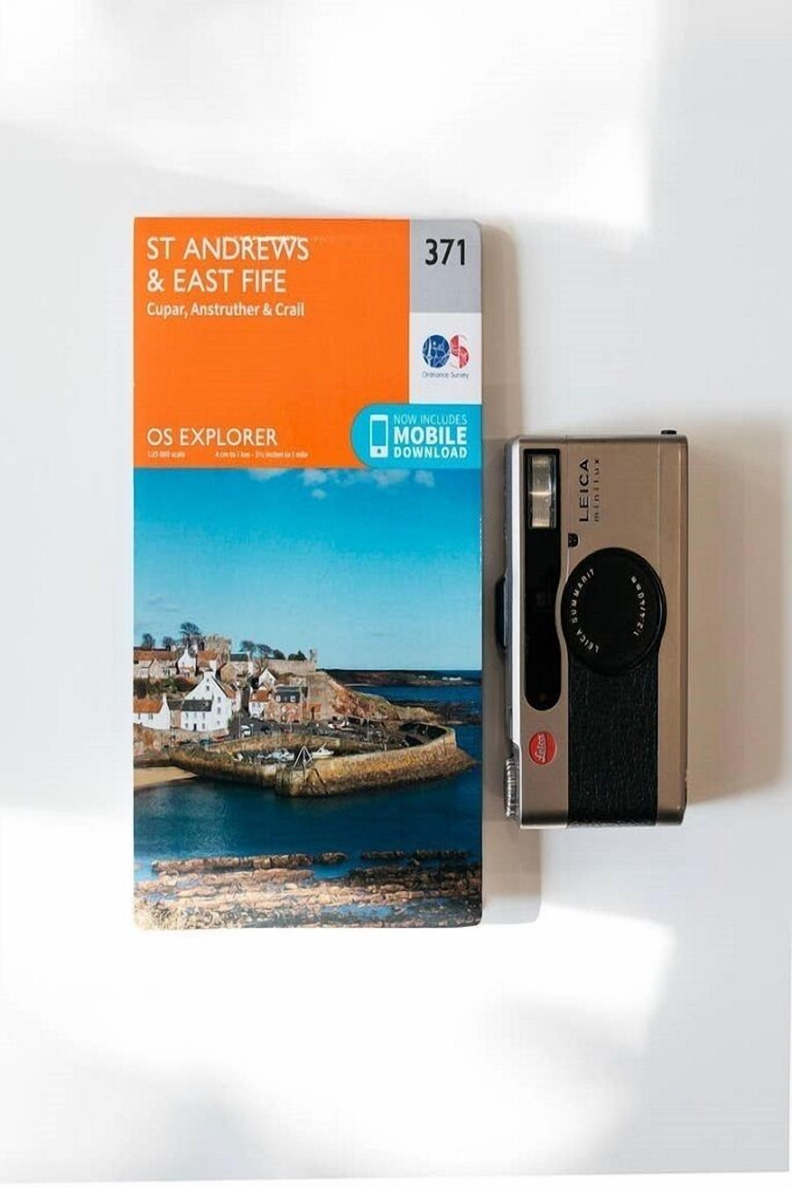 A Leica camera and a book titled 'OS EXPLORER' with a cover depicting a coastal scene.