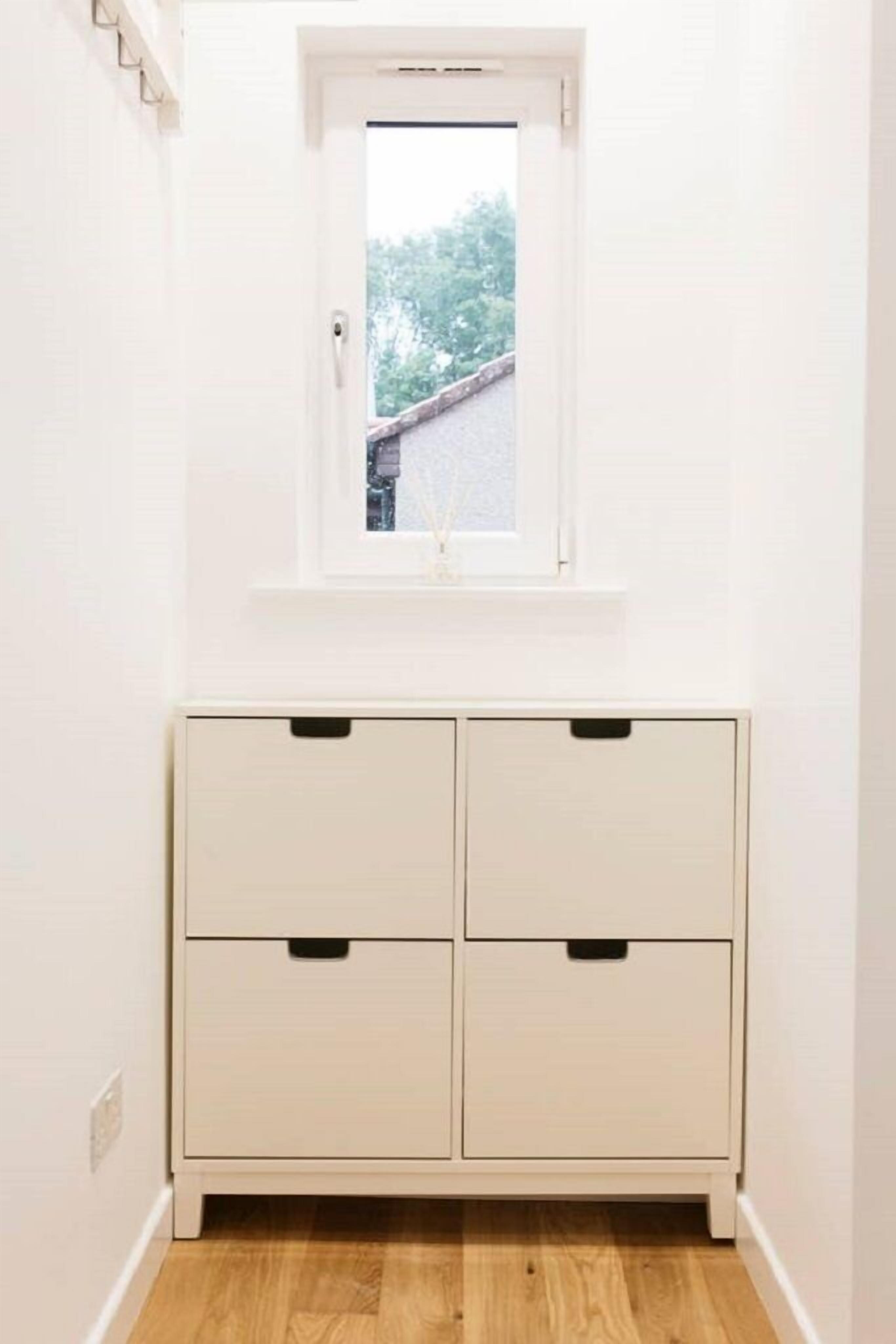 A narrow hallway with a white wall, a window, and a beige cabinet with two drawers.