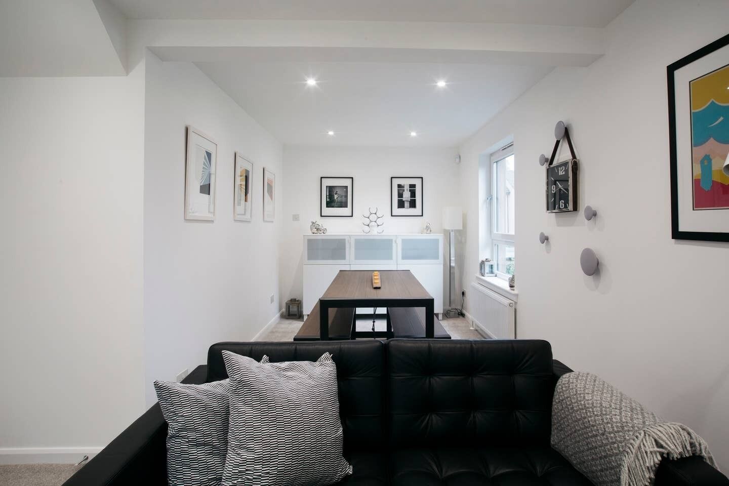 A modern living room with a black leather sofa, a dining table, and a kitchen in the background.