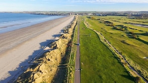 Vista aérea de una zona costera con playa, una carretera y campos verdes.