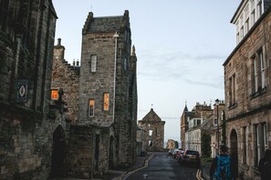 Una calle estrecha con edificios históricos de piedra, incluyendo una torre destacada y una iglesia con campanario.