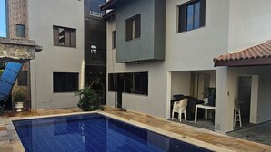 Una casa moderna de dos pisos con piscina, zona de estar exterior y patio cubierto.