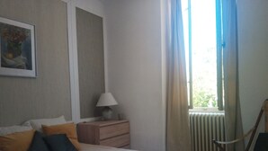 A bedroom with a bed, a nightstand, a lamp, a chair, and a window with curtains.