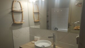 A modern bathroom with a wooden vanity, a round sink, a mirror, and a shower area.