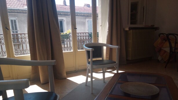 A room with a balcony, a table with a glass top, and a chair.