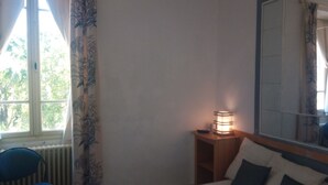 A bedroom with a bed, a chair, a bedside table with a lamp, and a window with curtains.