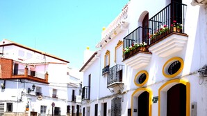 Una calle con edificios blancos, balcones con jardineras llenas de flores y un cielo azul despejado.