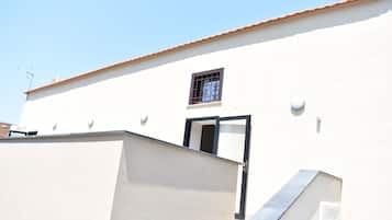 A white building with a tiled roof, a small window with metal bars, and a door.
