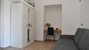 Une pièce avec un canapé gris, un bureau en bois avec une chaise et une armoire blanche.