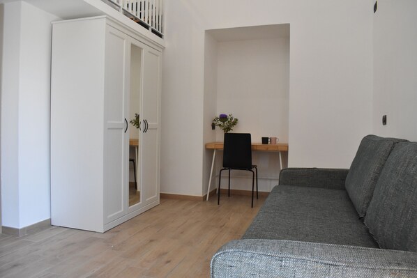 Une pièce avec un canapé gris, un bureau en bois avec une chaise et une armoire blanche.