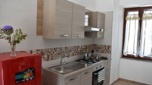 Une cuisine moderne avec un réfrigérateur rouge, des appareils en acier inoxydable et une fenêtre avec des rideaux.