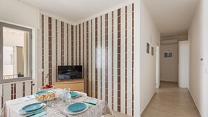 A dining area with a table set for four, a TV, and a striped wall. - Residence Kalura - Trilo con Balcone (SP) (Porto Cesareo)